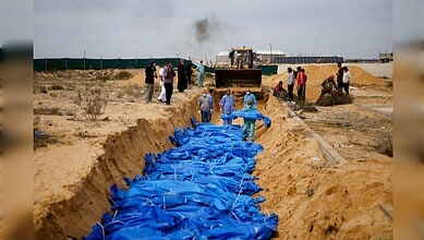 People bury victims in a trench with blue body bags in Gaza amid ongoing conflict.