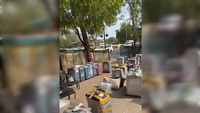 Outdoor scene with trees, parked cars, and scattered household items and containers.