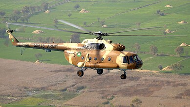 Military helicopter flying over green fields with hills in the background during daytime.