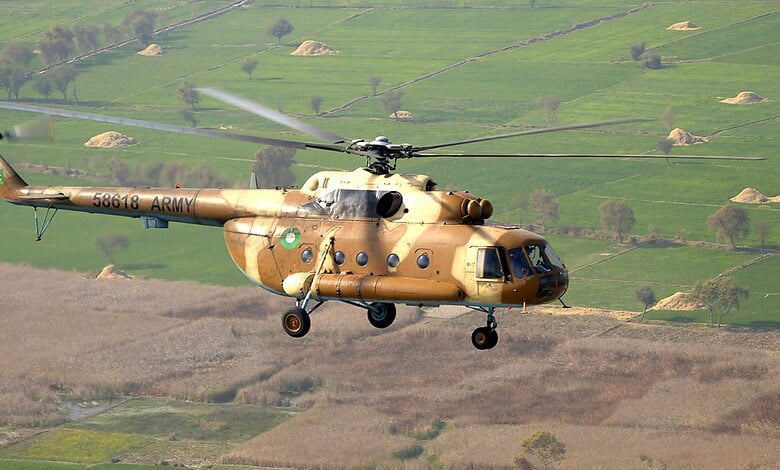 Military helicopter flying over green fields with hills in the background during daytime.