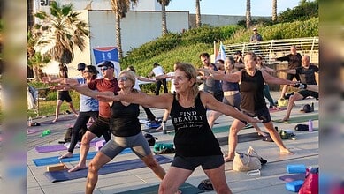 Group of diverse people practicing yoga outdoors in Jerusalem with flags and palm trees.