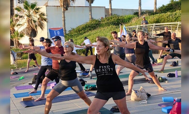 Group of diverse people practicing yoga outdoors in Jerusalem with flags and palm trees.