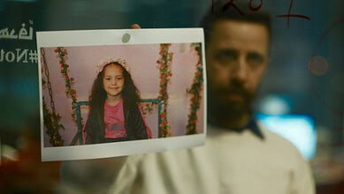 Young girl with curly hair smiling, holding a photo of herself on a decorated swing.