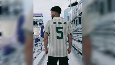 Young man wearing Hind Rajab cricket jersey with number 5 on a stadium walkway.