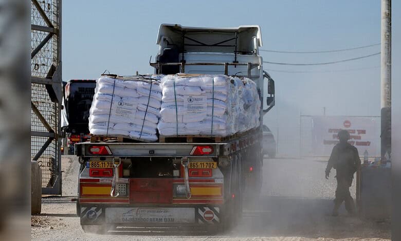 Heavy truck carrying cargo on dusty road with worker nearby in an industrial setting.