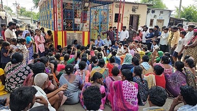 Large crowd gathered for a community meeting near a colourful building in India.