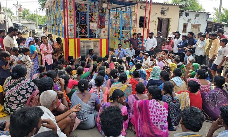 Large crowd gathered for a community meeting near a colourful building in India.