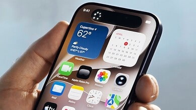 Smartphone displaying weather, calendar, and app icons, held in a person's hand against a blurred outdoor.