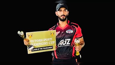 Cricket player in red uniform holding trophy and certificate, celebrating victory.