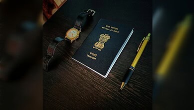 Indian passport, watch, and pen arranged on a dark wooden surface.