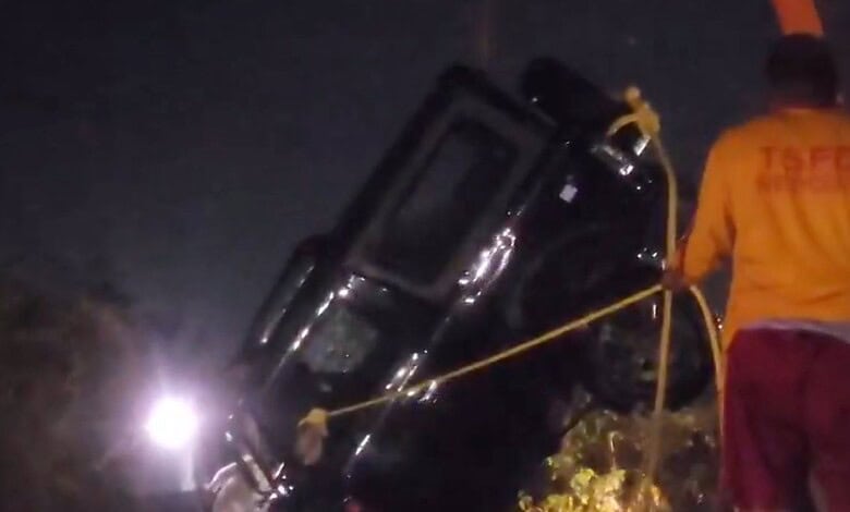 Emergency responders attending a nighttime car accident scene with a vehicle on its side.