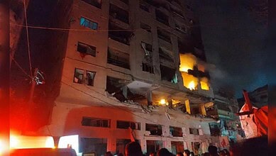 Nighttime building fire with flames and smoke coming from windows and balconies.