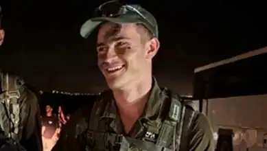 Israeli soldier smiling in uniform at night, possibly at a stadium or event.