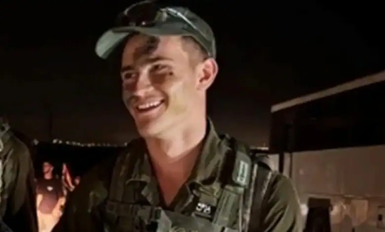 Israeli soldier smiling in uniform at night, possibly at a stadium or event.
