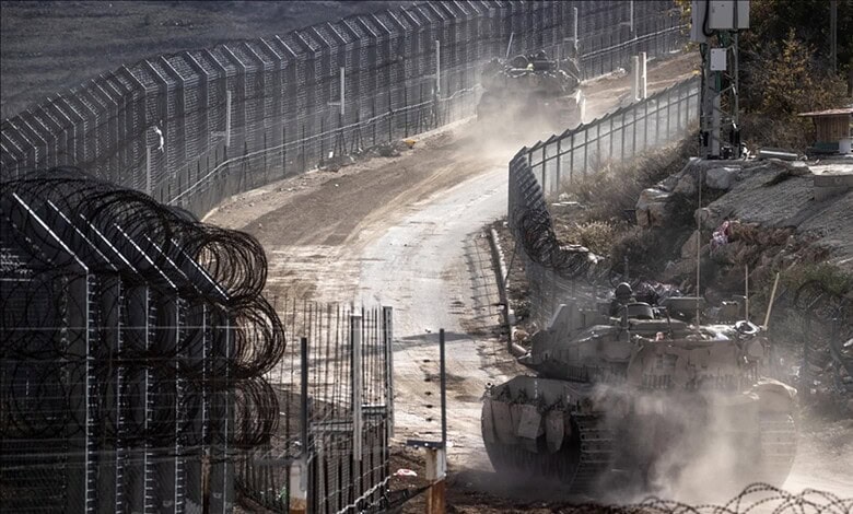 Tank moving on a dusty construction site with fencing and workers in the background.
