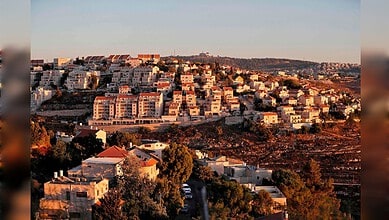 Sunset illuminates a hillside residential area with numerous houses and buildings in Siasat Daily image.