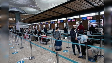 People waiting in line at Istanbul Airport check-in counters with luggage and masks.