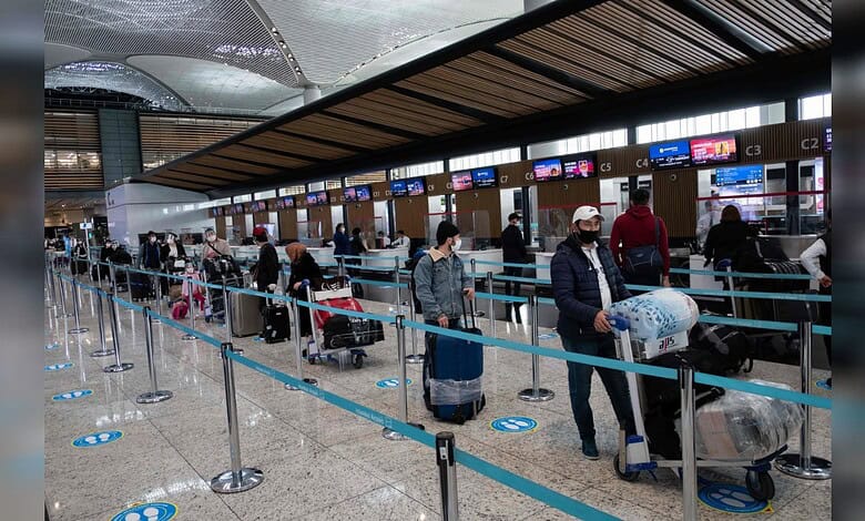 People waiting in line at Istanbul Airport check-in counters with luggage and masks.