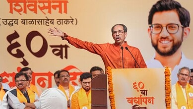 Indian politician addressing a rally with a large poster of a smiling man in the background.