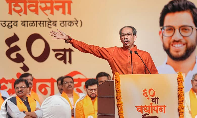 Indian politician addressing a rally with a large poster of a smiling man in the background.
