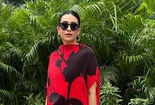 Karisma Kapoor in a red and black outfit with sunglasses, standing among green plants.