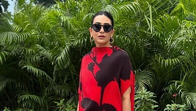 Karisma Kapoor in a red and black outfit with sunglasses, standing among green plants.