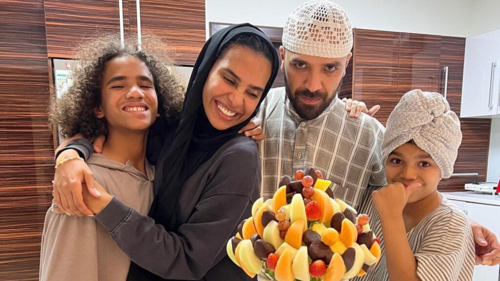 A woman and two children celebrating with a fruit cake in a modern kitchen.