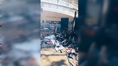 Damaged airport terminal interior with debris and burnt furniture following a fire incident.
