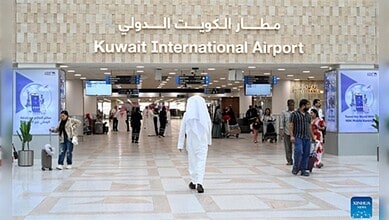 Interior of Kuwait International Airport with travelers and digital displays.