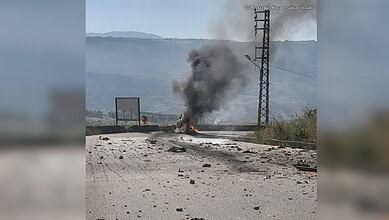 Fire and smoke emerging from a vehicle or object on the road, with electrical infrastructure in the backg.