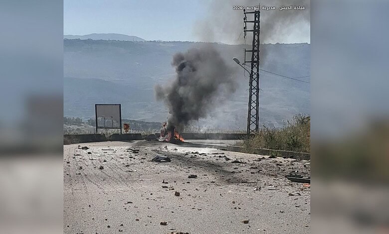 Fire and smoke emerging from a vehicle or object on the road, with electrical infrastructure in the backg.