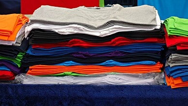 Colourful stacks of folded T-shirts in various colours on display at a market stall.
