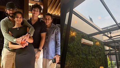 Group of four people smiling inside a modern glass house with greenery outside.