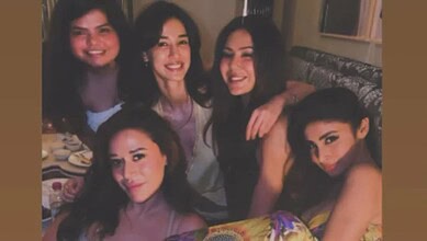 A group of five women smiling and enjoying a dinner together, showcasing friendship and happiness in a wa.