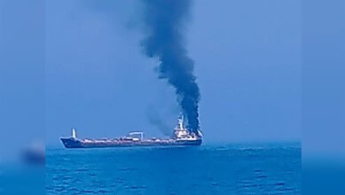 Oil tanker releasing thick black smoke into the sky while sailing on the ocean.