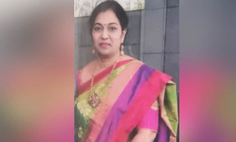 A woman in a colourful saree standing outdoors against a grey wall.