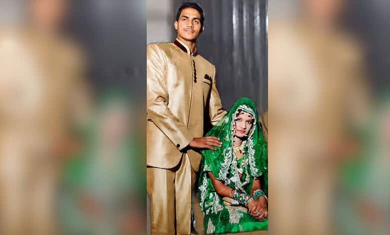 A young man in a gold sherwani standing beside a seated woman in vibrant green bridal dress and jewelry,.