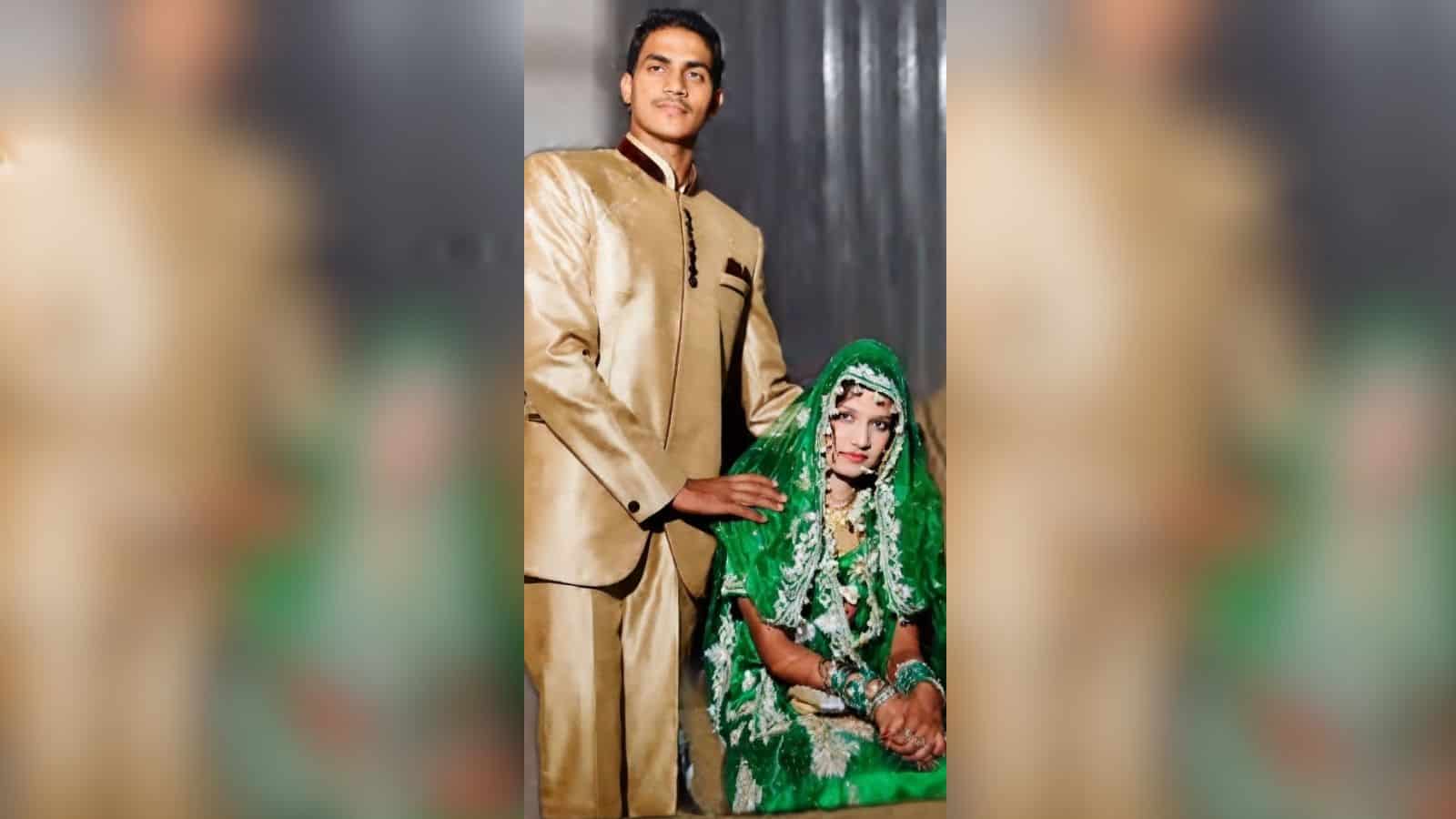 A young man in a gold sherwani standing beside a seated woman in vibrant green bridal dress and jewelry,.