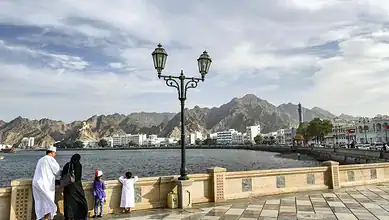 People enjoying the waterfront with mountains in the background and a cloudy sky.