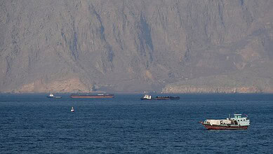 Multiple ships navigating in the Strait of Hormuz near mountainous terrain.