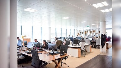 Open-plan office with employees working at desks and large windows letting in natural light.