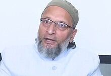 Owaisi, an Indian politician, speaking during a public event, wearing glasses and traditional attire.