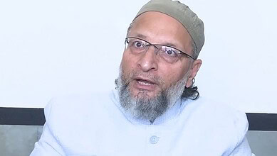 Owaisi, an Indian politician, speaking during a public event, wearing glasses and traditional attire.