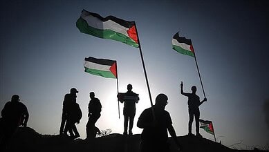 Silhouettes of people holding Palestinian flags against the sky in Gaza.