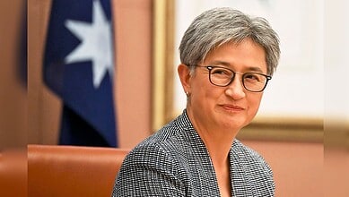 Australian Foreign Minister Penny Wong seated indoors during an official meeting, with a blurred Australian flag visible in the background.
