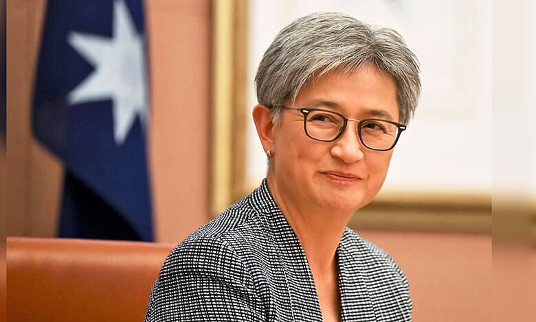 Australian Foreign Minister Penny Wong seated indoors during an official meeting, with a blurred Australian flag visible in the background.