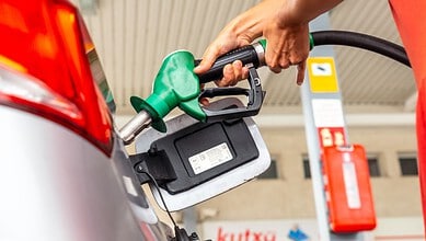 Person refuelling a car at a gas station with a green fuel nozzle.