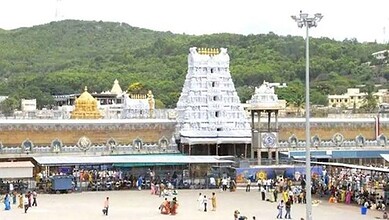 Crowd gathered outside Tirupati temple with temple tower in background.