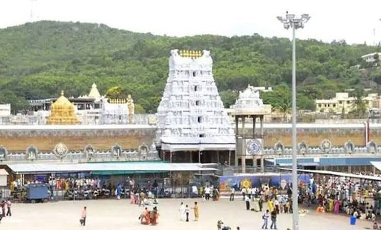 Crowd gathered outside Tirupati temple with temple tower in background.