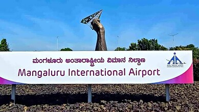 Mangaluru International Airport sign with a sculpture of a hand holding a satellite dish.